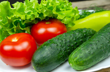 beautiful fresh, juicy vegetables on a white plate: fresh peppers, tomatoes, cucumbers, lettuce, dill