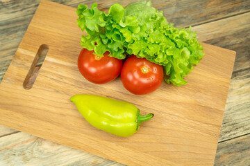 Fresh juicy vegetables peppers, tomatoes, cucumbers lettuce leaves with water drops are beautifully laid out on a wooden Board close-up. Vegetables are in the form of a funny face, top view