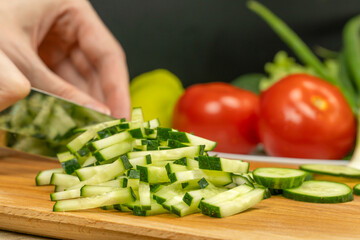 women's hands with a knife cut a cucumber on a cutting Board, next to a plate of vegetables