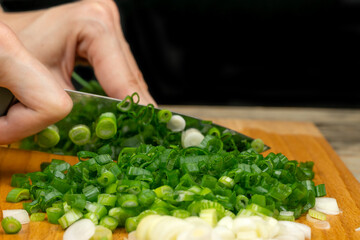 Female hands cutting green onions with a knife on a wooden Board close-up, back black background with copy space