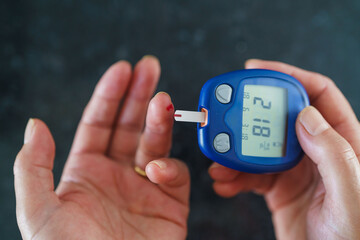 Medicine, Diabetes, Glycemia, Health care and people concept - close up of female using lancelet on finger to checking blood sugar level by Glucose meter