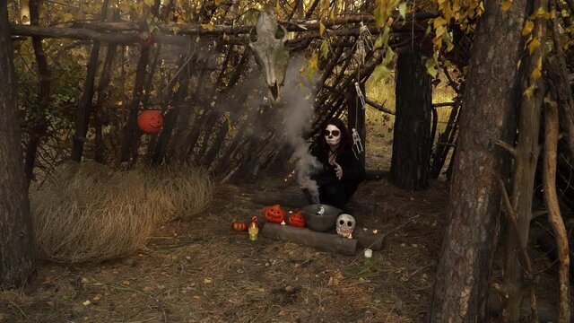 Witchcraft of a witch over a Smoking cauldron in a forest hut. Theme of the occult and esoteric rituals in the wild nature. Mystical wizard uses a cauldron to perform a magic ceremony.