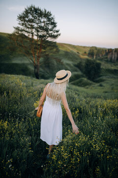 Girl in a white summer dress and hat on a background of beautiful nature on a hill in summer. Vertical photo