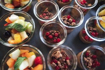 Top view of rows of transparent glass dishes with fruit salad and chocolate dessert. Celebration, party, birthday or wedding concept.