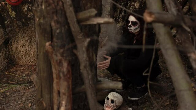 Witch with skeleton makeup does magic in the woods slow motion. Theme of the occult and esoteric rituals in the wild nature. Mystical wizard uses a cauldron to perform a magic ceremony.