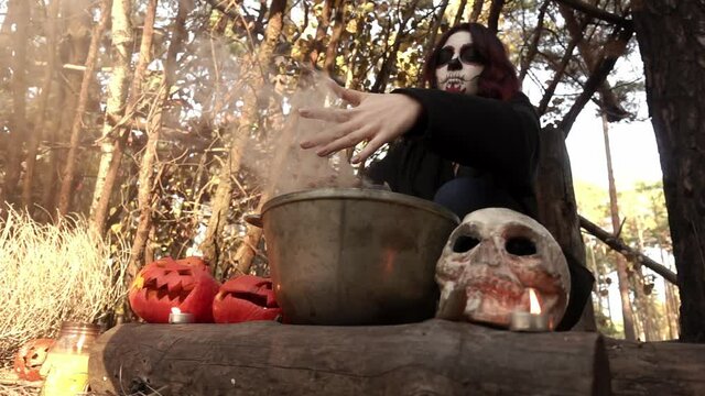 Witch girl plays with her hands with smoke from a pot of potion slow motion. Theme of the occult and esoteric rituals in the wild nature. Mystical wizard uses a cauldron to perform a magic ceremony.