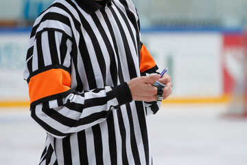 An ice hockey referee making notes on a small notebook during a game break.
