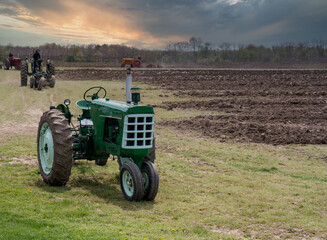 Obraz premium Group Tractors plowing at sunset, farmers helping out each other
