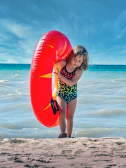 Little girl on the beach carries a large blow up inner tube