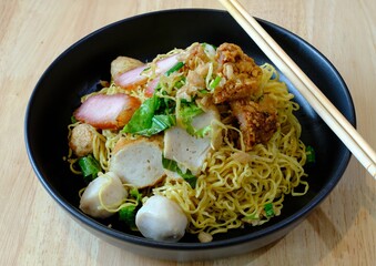 egg noodle with grilled pork and fish ball,Thai style,black blow on wooden table