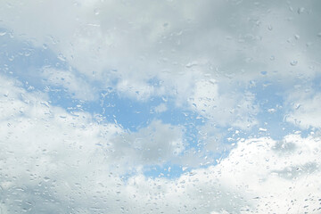 Fototapeta premium Raindrops on the window glass. Clear blue sky with white clouds. Blurred background.