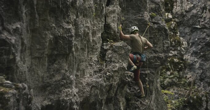 Climber climb up ascend reach with hand and attach clip lead rope in quickdraw carabiner chalk bag wear helmet in stone rock wall slow motion