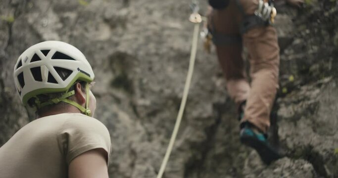Climber with helmet mustache smile protect watching rock climb partner for safety belay rope outdoors lifestyle sport in nature close up over shoulder