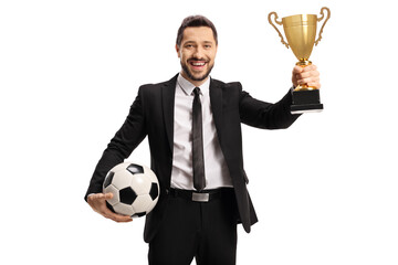 Man in a suit holding a trophy cup and a soccer ball