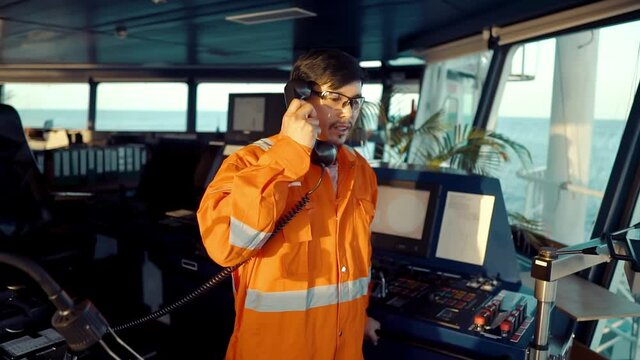 Filipino deck Officer on bridge of vessel or ship wearing coverall during navigaton watch at sea . He is speaking on GMDSS VHF radio, communication between vessels.