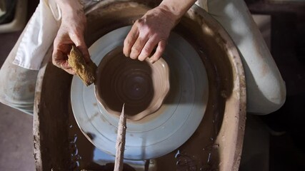 Overhead close up of male potter shaping clay for bowl on pottery wheel in ceramics studio - shot in slow motion