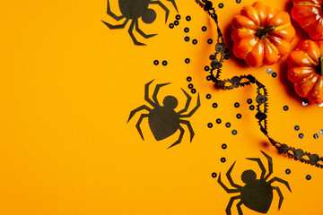 Halloween party concept. Flat lay composition with pumpkins, black spiders, confetti, ribbon on orange background. Top view, overhead.