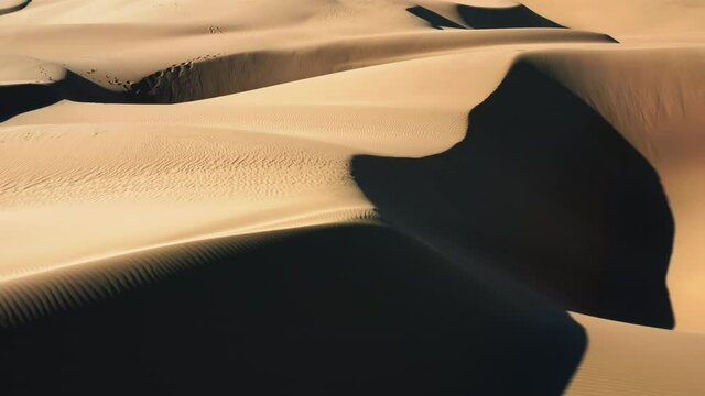 4K close up view on the sand waves with deep and long shadows at sunset. Beautiful ripples texture on the sand hills. Aerial view drone flying over the scenic landscape of massive golden dunes, USA