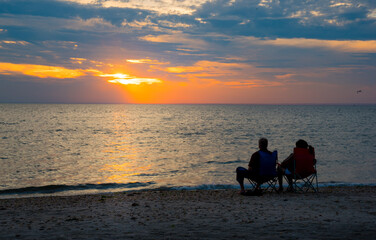 Obraz na płótnie Canvas A senior couple in beach chairs enjoying beautiful sunset at a beach. 