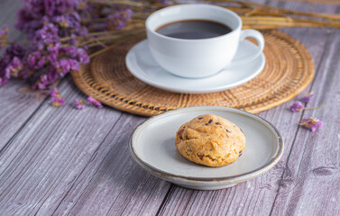 Close-up of a cookie on a plate with a white coffee cup and flower blurred background.