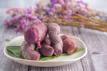 Pile of ripe purple yams is placed on a plate on a wooden table