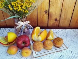 Obraz na płótnie Canvas Food still life on the kitchen table a vase of wild flowers apples apricots sponge cakes lemon orange cookies in a basket