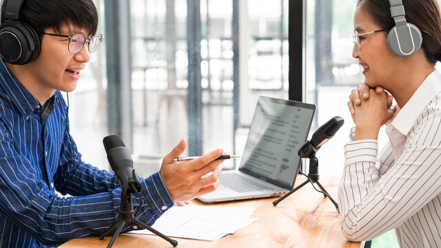 Asian woman radio hosts gesturing to microphone while interviewing a man guest in a studio while recording podcast