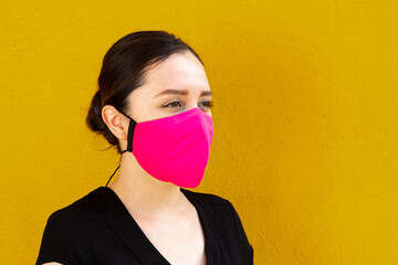 Woman wearing a pink facemask, side shoot, outdoors with bright yellow background