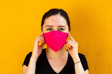 Woman wearing a pink facemask, outdoors with bright yellow background