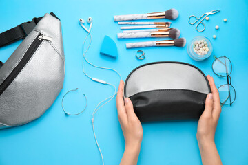 Female hands and bag with decorative cosmetics on color background
