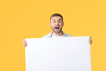 Excited young man with blank placard on color background