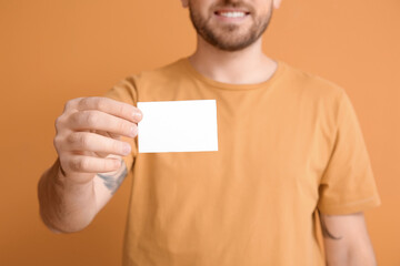 Young man with blank business card on color background, closeup