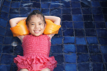 Asian child cute or kid girl smile lying or sleep on swimming pool and wear armband or life jacket...