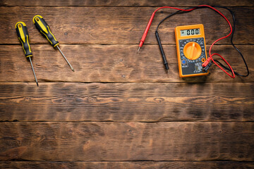 Multimeter and screwdrivers on the wooden workbench background with copy space.