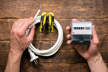 Electrician is holding an electricity meter on a wooden flat lay workbench background.