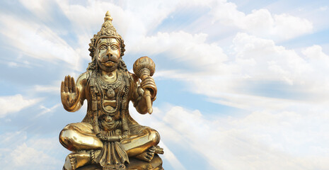 Fototapeta premium Bronze Hanuman on the background of light cloudy sky.