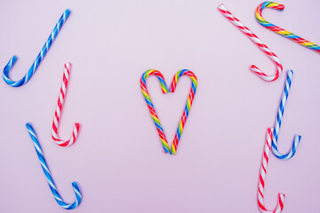 lot of multi-colored candy canes and one in the form of a heart on a pink background, copy space