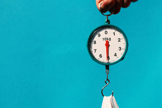 Round spring scales on a blue background show exactly five kilograms. A man is weighing a package.