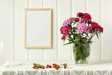 empty frame on the wall, bouquet of Turkish carnations and garden strawberries.