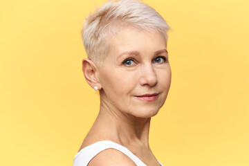 Half profile shot of beautiful middle aged European woman with blue eyes, short dyed hair and face wrinkles posing in studio having confident look. People, maturity, aging and lifestyle concept