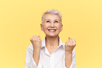 Studio shot of beautiful energetic mature businesswoman with pixie hairstyle exclaiming Yes,...