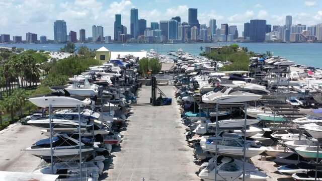 4K aerial view on an elevator truck driving between high rows of multi-level yacht parking lot. Beautiful slow motion drone video for boat business. Marine club with Miami downtown on background