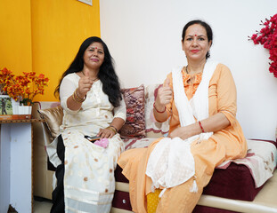 Two mid aged indian women showing thumbs up in the camera.