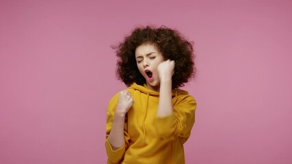 Enthusiastic happy joyful girl afro hairstyle in hoodie shouting, raising fists in gesture I did it, celebrating success, winning and goal achievement concept. studio shot isolated on pink background