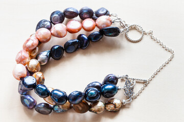 handmade bracelet from three stings of dyed natural river pearls and silver chain and clasp closeup on pale wooden table