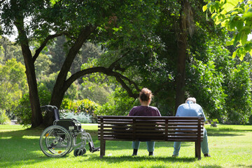 Older couple with wheelchair sitting on bench in park in Melbourne, Australia