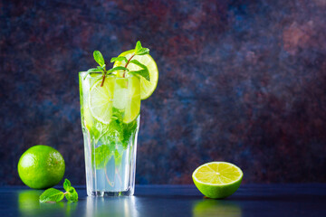 Mojito cocktail with lime and mint in tall glass. Fresh mojito in glass on a dark background. Refreshing mint cocktail with lime. Infused water
