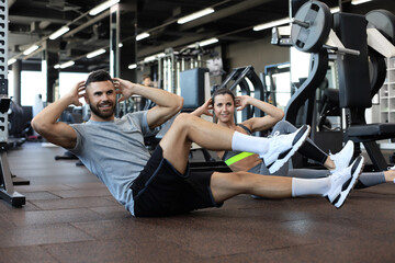 Attractive man and woman working in pairs performing sit ups in gym.