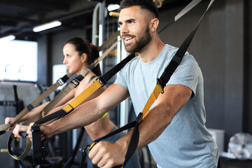 Young couple on body training with trx in gym.