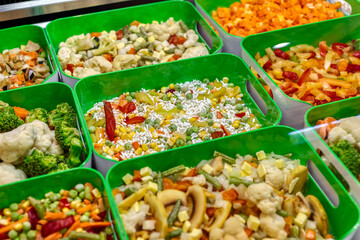 Frozen vegetables, fruits and berries. Food products are poured into rectangular plastic trays.